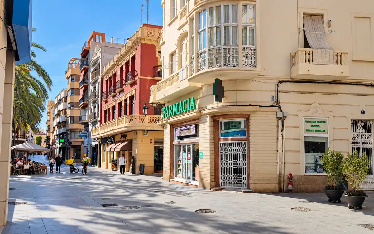 Calle peatonal del centro de Elche con comercios, terrazas y palmeras.
